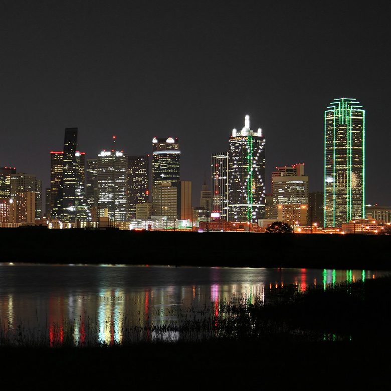 A vibrant city skyline at night, illuminated lights reflecting beautifully on the calm water below.