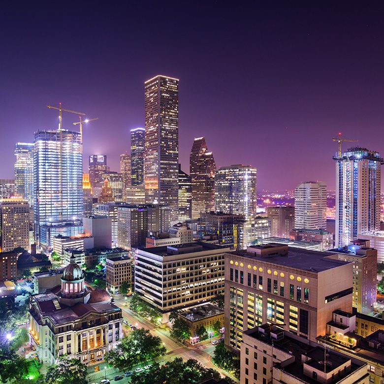 Houston skyline illuminated at night, showcasing tall buildings and a vibrant cityscape against a dark sky.