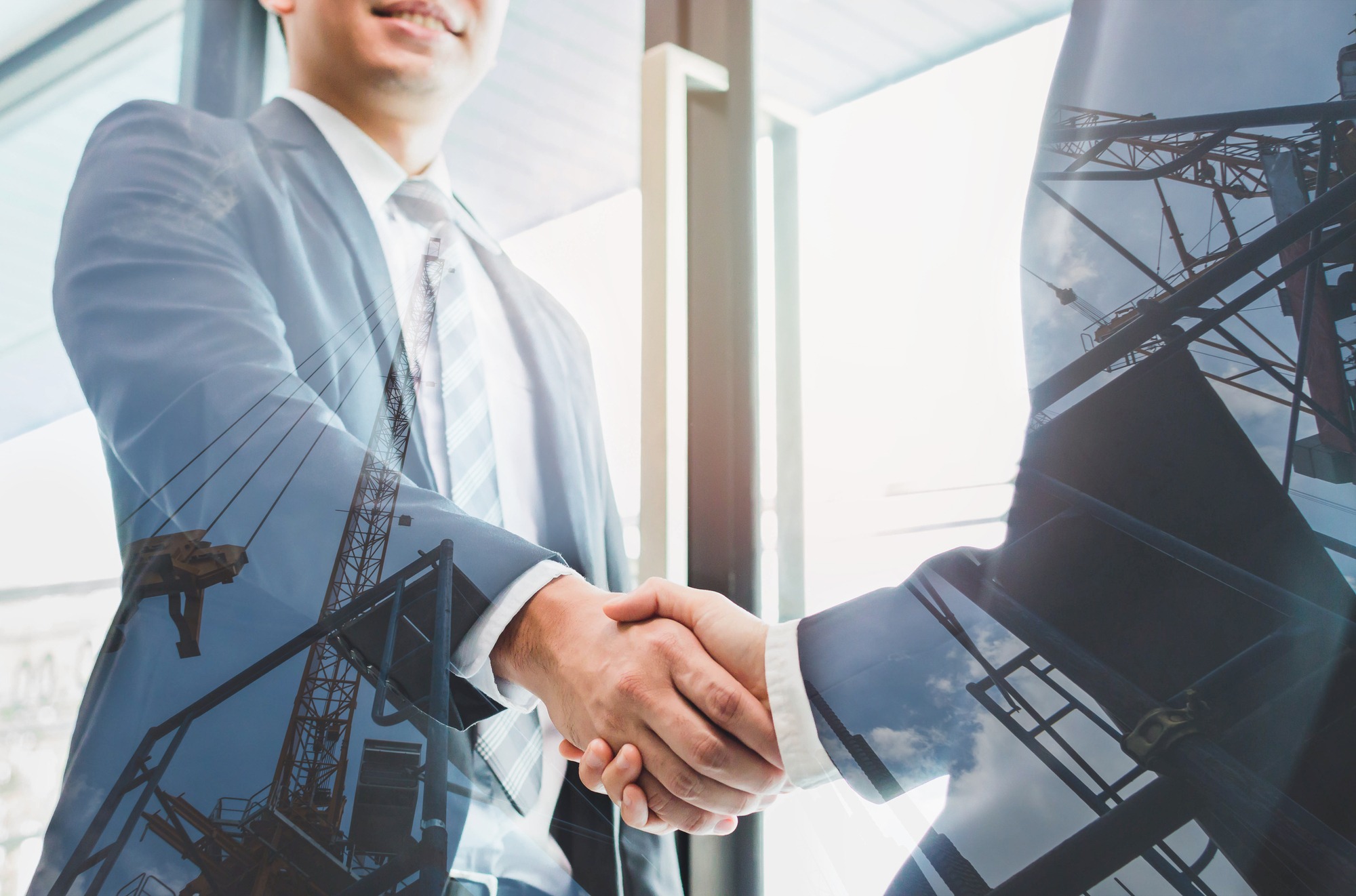 Double exposure of two businessmen reaching an agreement and making handshake with abstract construction site - Greeting and dealing real estate business concepts.
